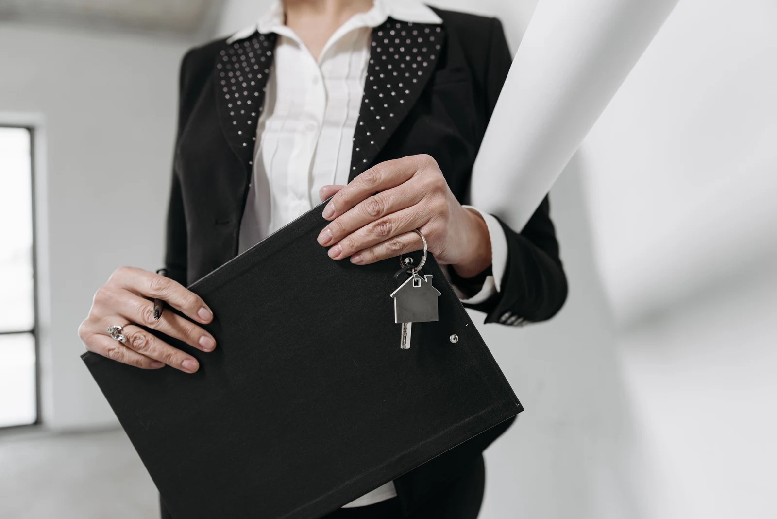 Woman in business attire holding a portfolio with a house key