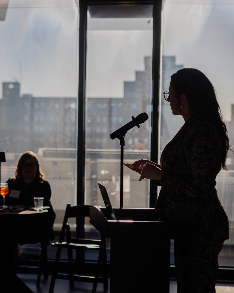 Stephanie Armstrong standing at a microphone in a window-lit room